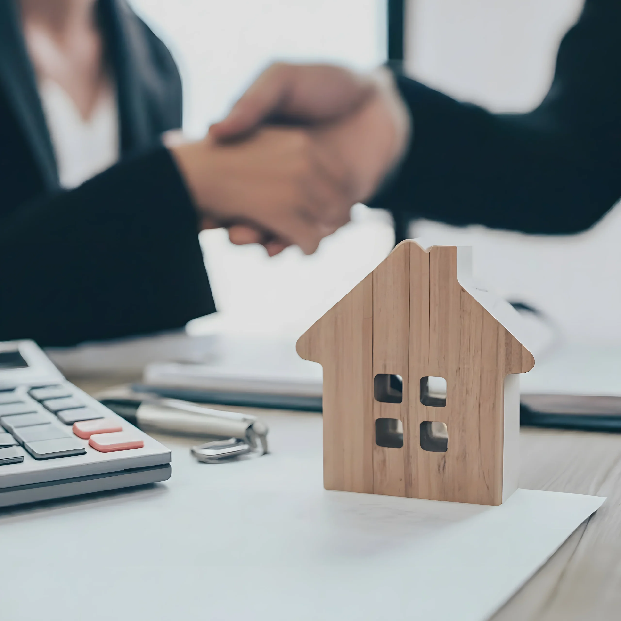 Poignée de main immobilière avec maison en bois et calculatrice